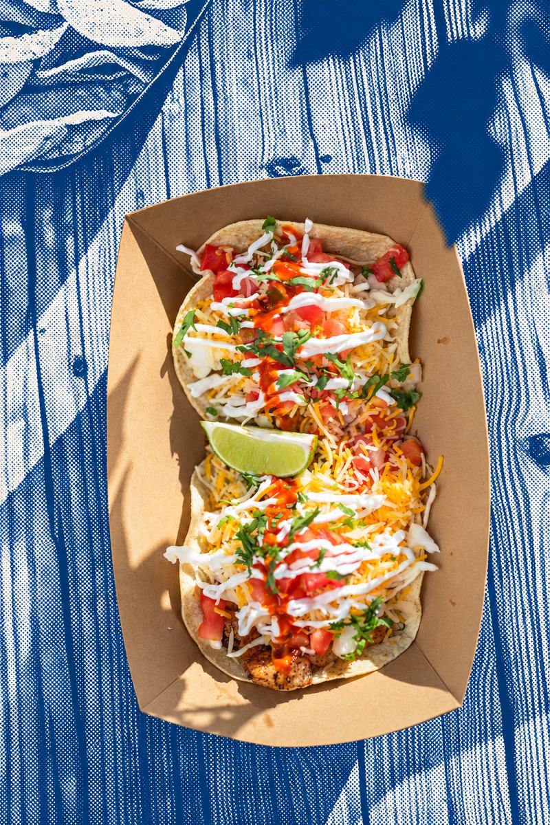 The Original fish tacos with pico, cheese and a lime wedge in a paper boat